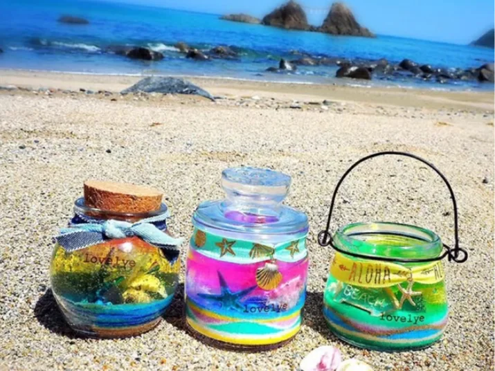 色砂を重ねて作った3つのジェルキャンドルサンドを海辺に並べた様子
