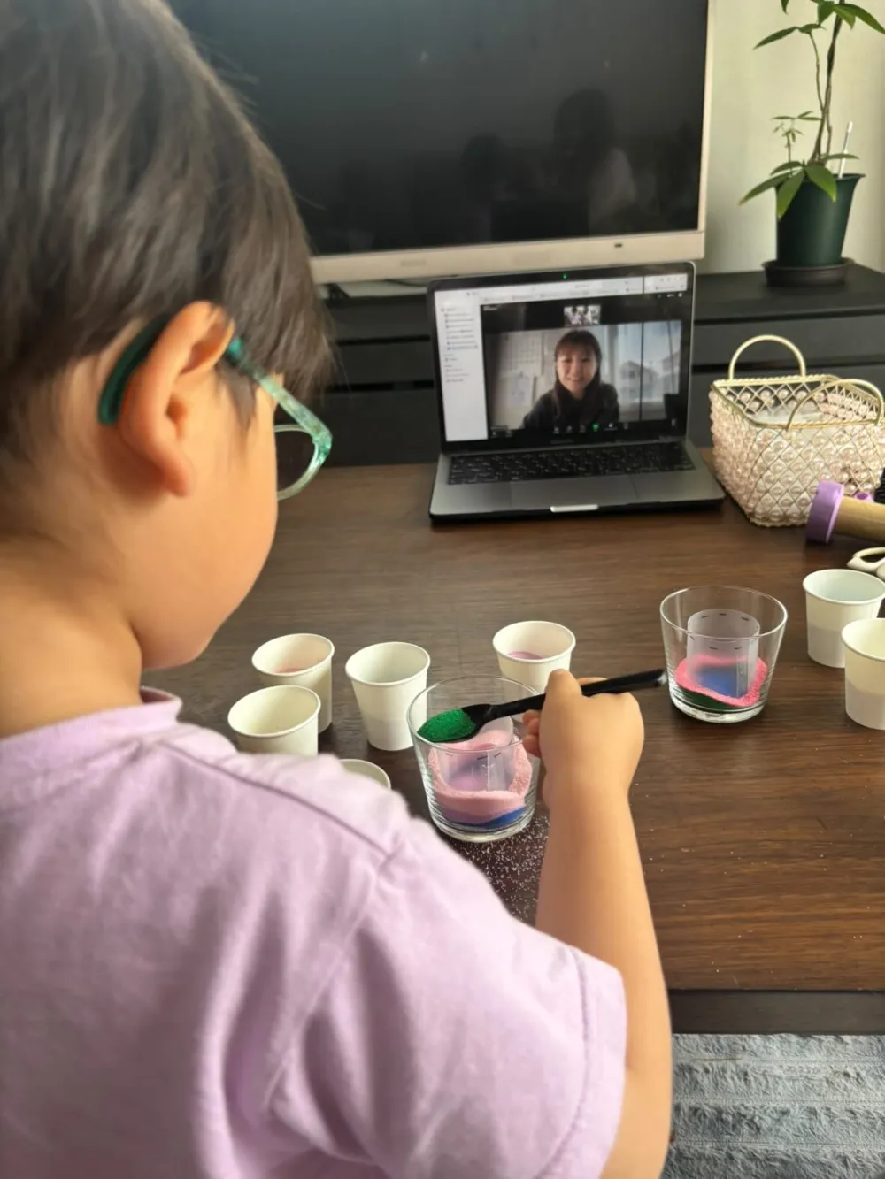 パソコン画面の講師を見ながら色砂をスプーンで入れる4歳の男の子